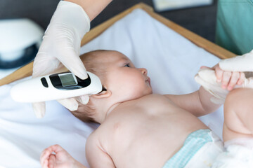 Female pediatrician with digital infrared thermometer measuring baby girl patient's ear temperature
