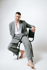 Man in grey costume sits on the chair, barefoot. In studio, fashion