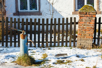 Old water column with blue cracked paint near the house on a winter day.