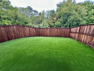 a beautiful backyard with green grass surrounded by a wood fence in a cloudy day with forest in the background.