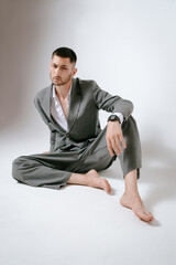 Handsome man in grey suit sits on the floor barefoot