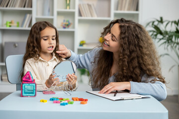 Naklejka premium Cute long-haired girl exercising with a mirror at the speech therapist office