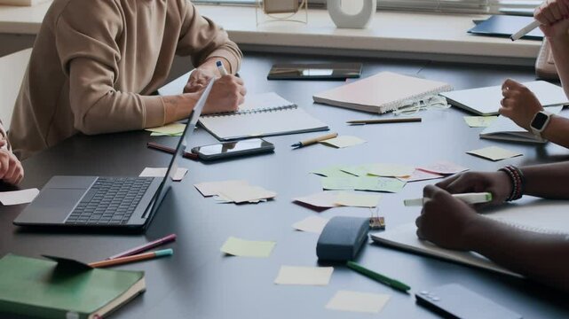 Cropped shot of group of multiethnic adult students using colorful sticky notes on desk while studying English vocabulary during interactive lesson in classroom