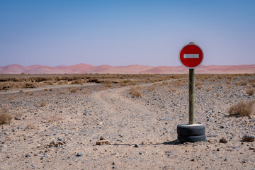 A no-entry sign stood in two old tyres at the start of a road that disappears towards pink and orange sand dunes in the distance in Sossusvlei, Nambia