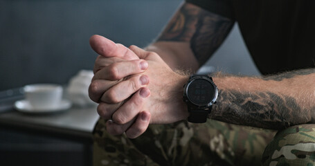 Close up of nervous military man in uniform sitting and clenching hands during therapy session with...