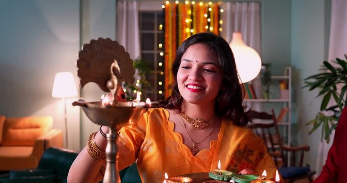Joyful Indian Asian married couple dressed in traditional attire lighting diya or samai to celebrate Diwali festival at night, surrounded by festive decor, vibrant lighting in a beautifully adorned