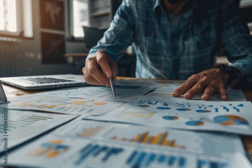 Poster A person sitting at a table with papers and a laptop, ideal for business or finance-related projects