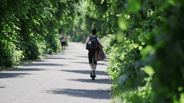 A group of people are walking and riding a bike down a path in a pubic park in Cologne, Germany. The path is surrounded by trees and bushes, and there are several bicycles parked along the path