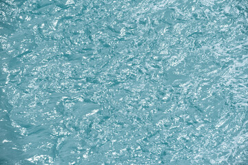Blue water with ripples on the surface. Defocus blurred transparent blue colored clear calm water surface texture with splashes and bubbles. Water waves with shining pattern texture background.