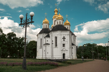 Surrounded by green trees and a vibrant sky, the church's golden domes shine brightly. The scene exudes both spiritual significance and architectural beauty.