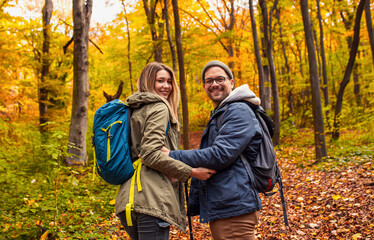 Portrait of smiling couple with backpacks hiking together in forest looking at camera.