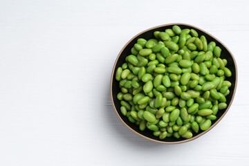 Fresh edamame soybeans in bowl on white wooden table, top view. Space for text