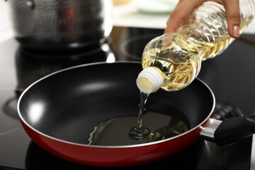 Woman pouring oil into frying pan on cooktop in kitchen, closeup