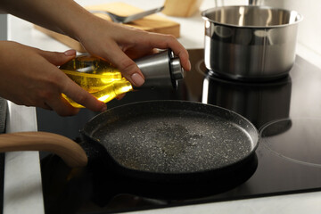 Woman with bottle of oil and frying pan in kitchen, closeup