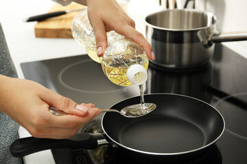 Woman pouring oil into spoon over cooktop in kitchen, closeup