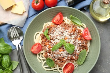 Delicious pasta bolognese with basil and tomatoes served on grey table, flat lay