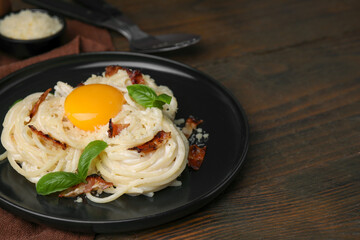Delicious pasta Carbonara with egg yolk, bacon and basil on wooden table, closeup