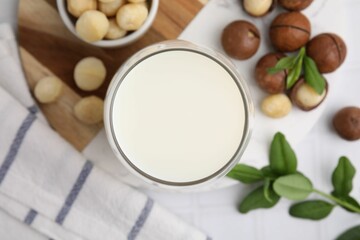 Glass of macadamia milk and nuts on white tiled table, flat lay