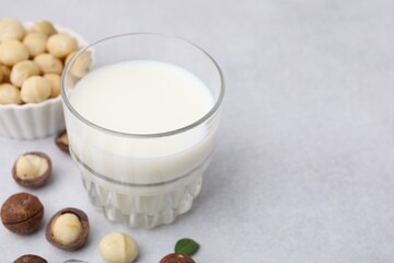 Glass of macadamia milk and nuts on white table, closeup. Space for text