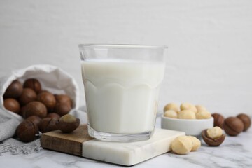 Glass of macadamia milk and nuts on white marble table, closeup