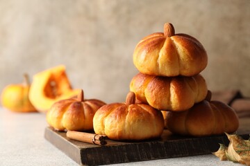 Tasty pumpkin shaped buns and cinnamon on light grey table, closeup