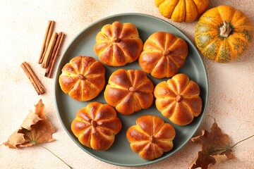 Tasty pumpkin shaped buns, ingredients and dry leaves on beige textured table, flat lay
