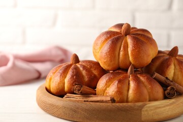 Tasty pumpkin shaped buns and cinnamon sticks on white table, closeup