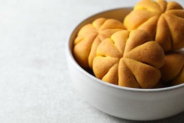 Tasty pumpkin shaped buns in bowl on grey table, closeup. Space for text