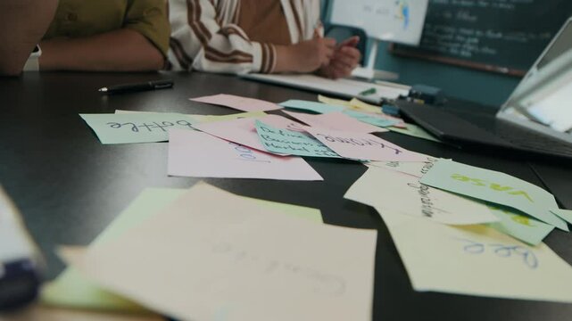 Cropped shot of unrecognizable multiracial adult students playing interactive linguistic game with sticky notes while studying together in modern classroom