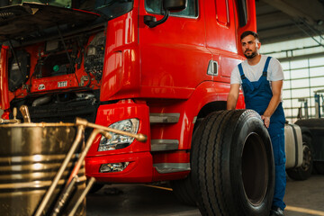 Worker in truck service is replacing a tire on a large red truck. Scene captures the hard work and dedication involved in vehicle maintenance.
