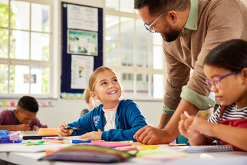 Happy little girl asks teacher for help in elementary classroom