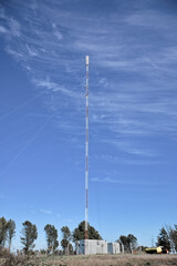 Obraz premium Tall TV communication tower with antennas against a blue sky and green field