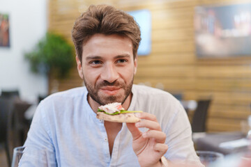 Smiling man eating sandwich in cafe - Healthy lifestyle and casual dining portrait