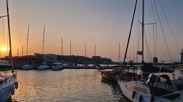 Serene sunset at a harbor with boats docked in calm waters. The statue of Saint Nicholas the patron of sailors, and the famous windmill on the horizon in the old town of Nessebar, Bulgaria