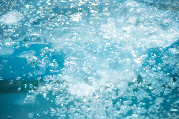 Blue water with ripples on the surface. Defocus blurred transparent blue colored clear calm water surface texture with splashes and bubbles. Water waves with shining pattern texture background.