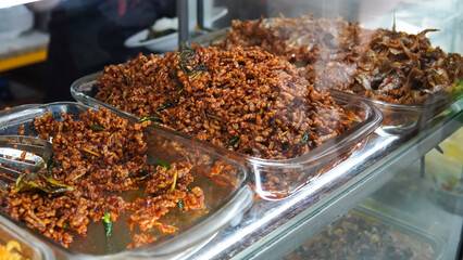 Food stalls called warteg share a variety of buffet traditional menus of indonesia with vegetables, chicken curry sauce, beef, eggs, tofu, tempeh. Menu in glass display case. 