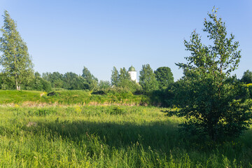 sunny landscape with stone walls among grass, ruins of ancient fortifications and a castle tower in the distance
