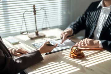 Lawyer explaining agreement to client signing contract with gavel and scales of justice visible