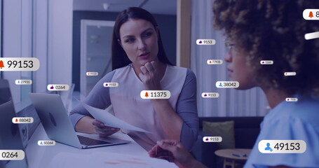 Image of social media icons with numbers over diverse colleagues discussing work in office