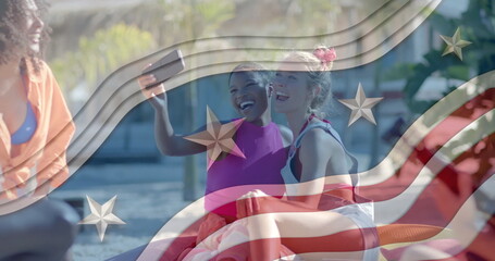 Image of american flag elements over happy diverse female friends taking selfies on sunny beach
