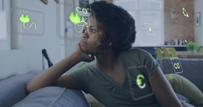 Image of eco icons and data processing over african american woman on sofa at home