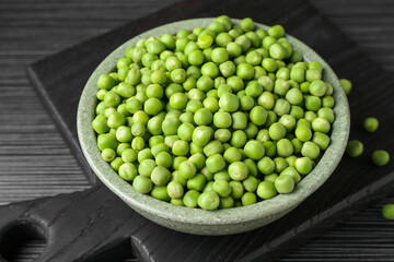 Fresh green peas in bowl on black wooden table, closeup
