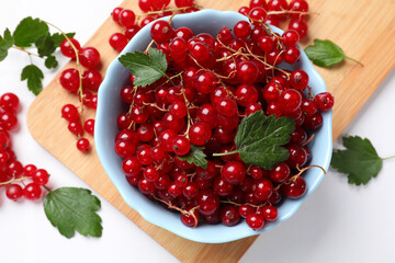 Fresh red currants in bowl and green leaves on white table, top view