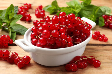 Fresh red currants in bowl and mint on wooden table, closeup