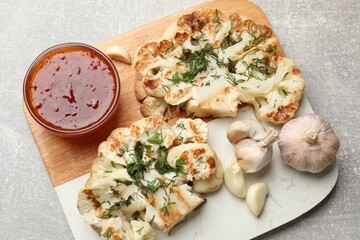 Delicious grilled cauliflower steaks with sauce and garlic on grey table, above view