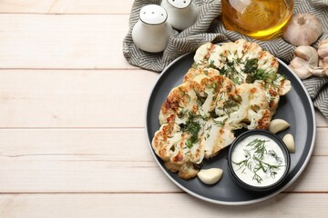 Delicious grilled cauliflower steaks with sauce, garlic and dill on wooden table, flat lay. Space for text