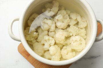 Cauliflower in pot with water on white marble table, above view