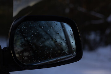 The car mirror reflects a serene winter landscape with water droplets, adding unearthly beauty to the tranquil scene. Fairytale winter forest reflected in the car mirror.