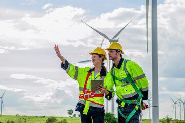 Two workers in yellow and black safety gear are standing next to a wind turbine