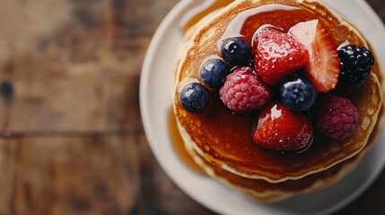 A stack of pancakes topped with fresh berries and syrup on a wooden table.